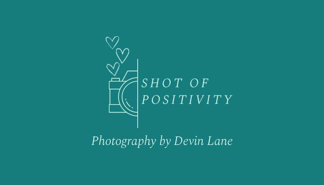 Brand logo for Shot of Positivity Photography by Devin Lane: teal background with a white outlined camera and three hearts, and elegant script text.